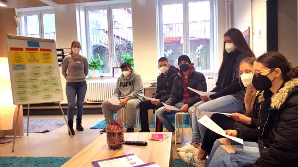 Schülerinnen und Schüler sitzen im Ausstellungsraum, im Hintergrund Teppichböden