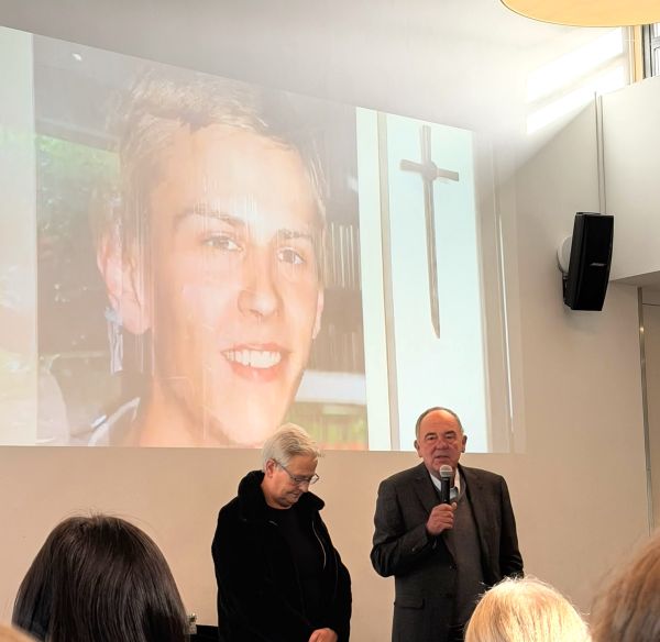 Das Ehepaar Holze vor dem Bild ihres Sohnes Tilman. Auf dem Bild ist außerdem ein Kreuz als Zeichen dafür, dass Tilman gestorben ist.