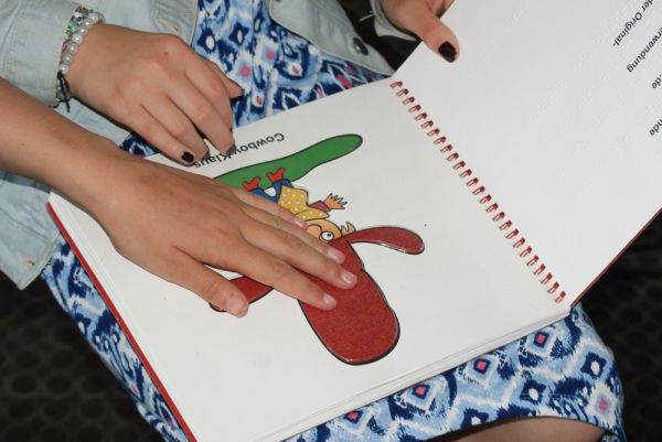 eine Seite aus einem Buch für blinde Menschen, eine Kinderhand ertastet die Abbildung