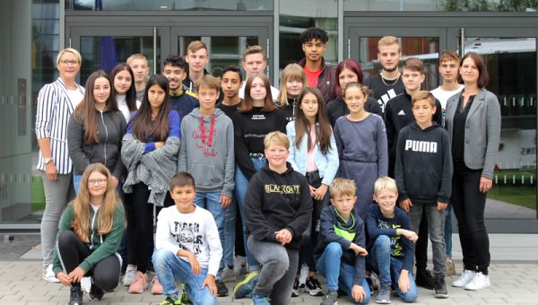 Die Schülervertreter und zwei Lehrerinnen stehen vor einer Glastür.