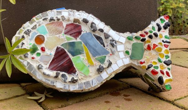 ein gebastelter Fisch, der mit bunten Mosaiksteinen aus Spiegel, Glas und Fliesenscherben verziert ist